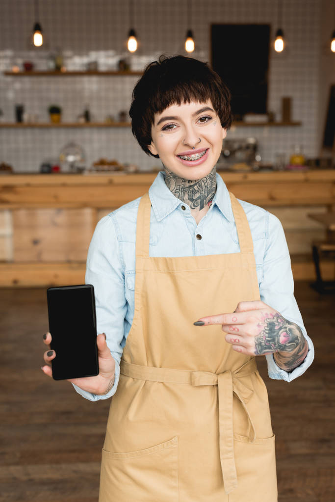 весела офіціантка, що вказує пальцем на смартфон з порожнім екраном
 - Фото, зображення
