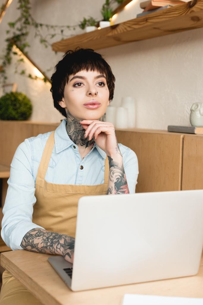 мечтательная официантка, пользующаяся ноутбуком в кофейне и отворачивающаяся
  - Фото, изображение