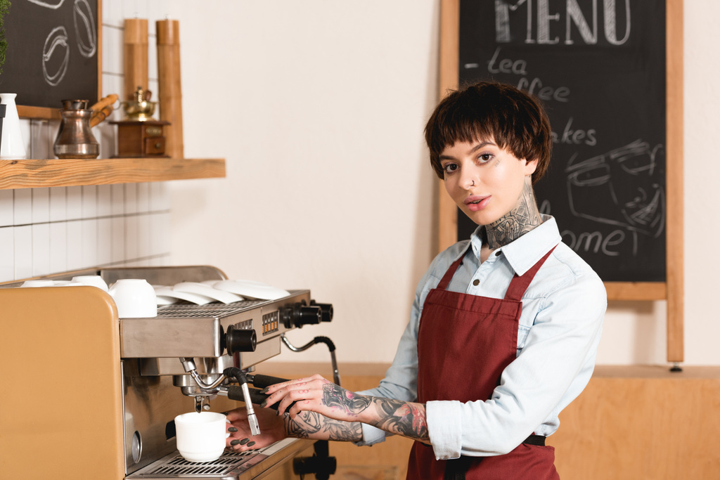 pěkně potetovaný barista Příprava kávy v kávovaru a při pohledu na fotoaparát - Fotografie, Obrázek