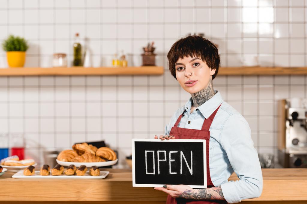 attractive barista holding signboard with open lettering and looking at camera - Photo, Image