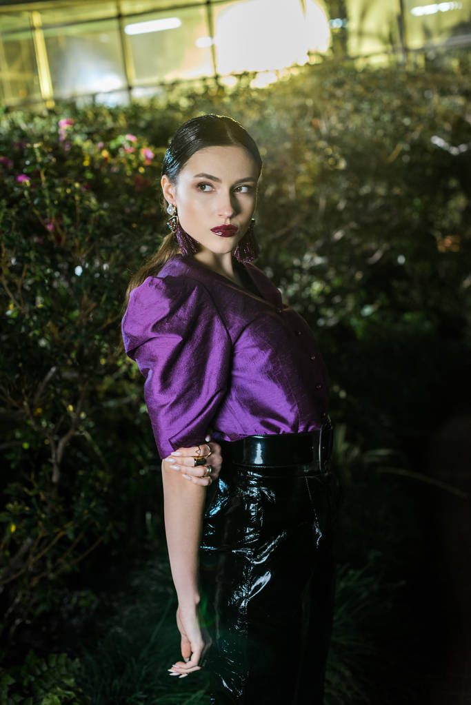 Pensive girl in purple blouse and leather pants posing in orangery - Photo, Image