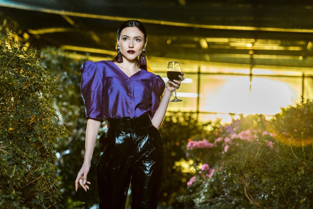 atemberaubende junge Frau in lila Bluse mit Weinglas in der Orangerie - Foto, Bild