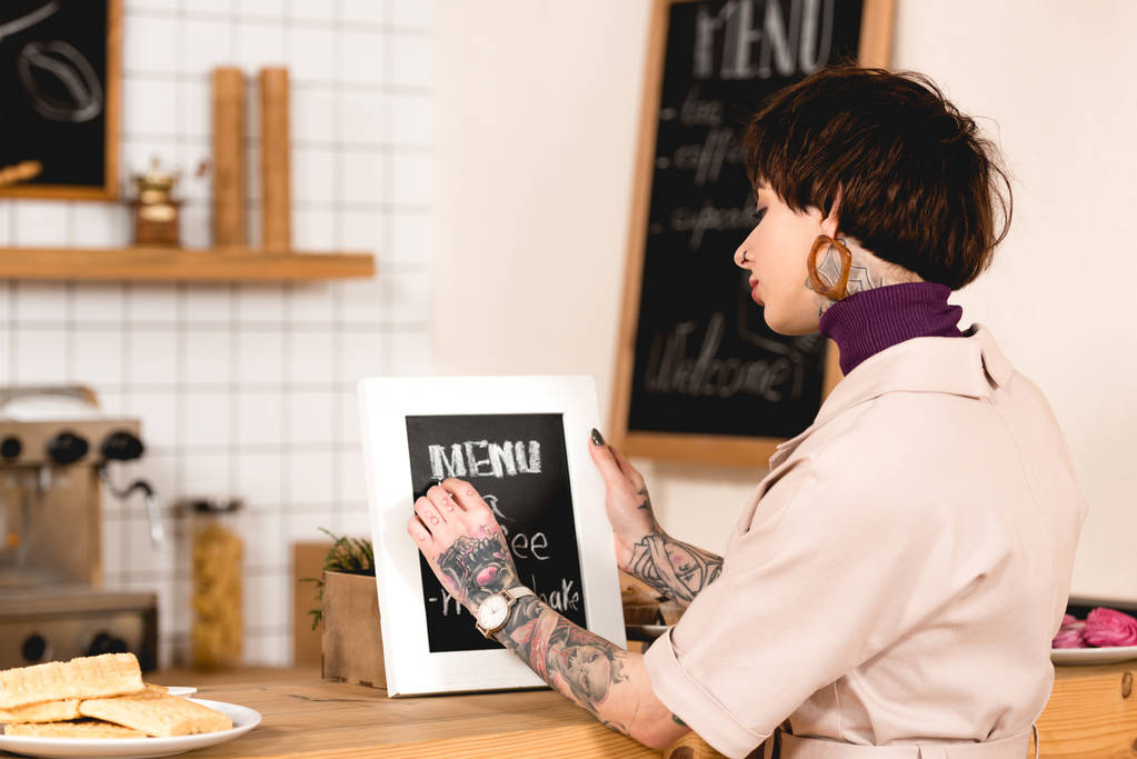 mooie zakenvrouw schrijven op menu bord terwijl staande aan de toog - Foto, afbeelding