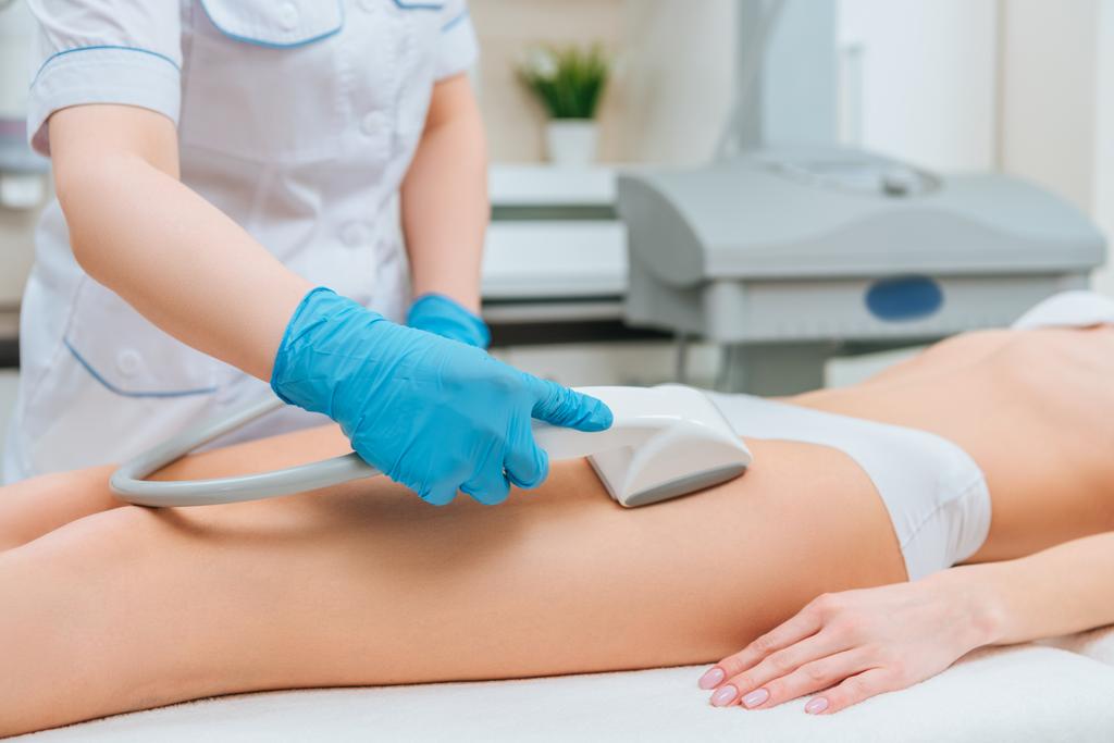Vista cortada de cosmetologista com rolo fazendo massagem starvac perna
 - Foto, Imagem