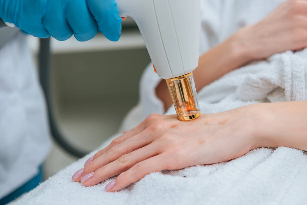 Vista cortada de cosmetologista em luvas de borracha fazendo tratamento a laser
 - Foto, Imagem