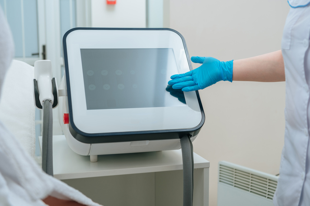 Vista parcial del cosmetólogo en guante de goma tocando la máquina láser en la clínica
 - Foto, imagen