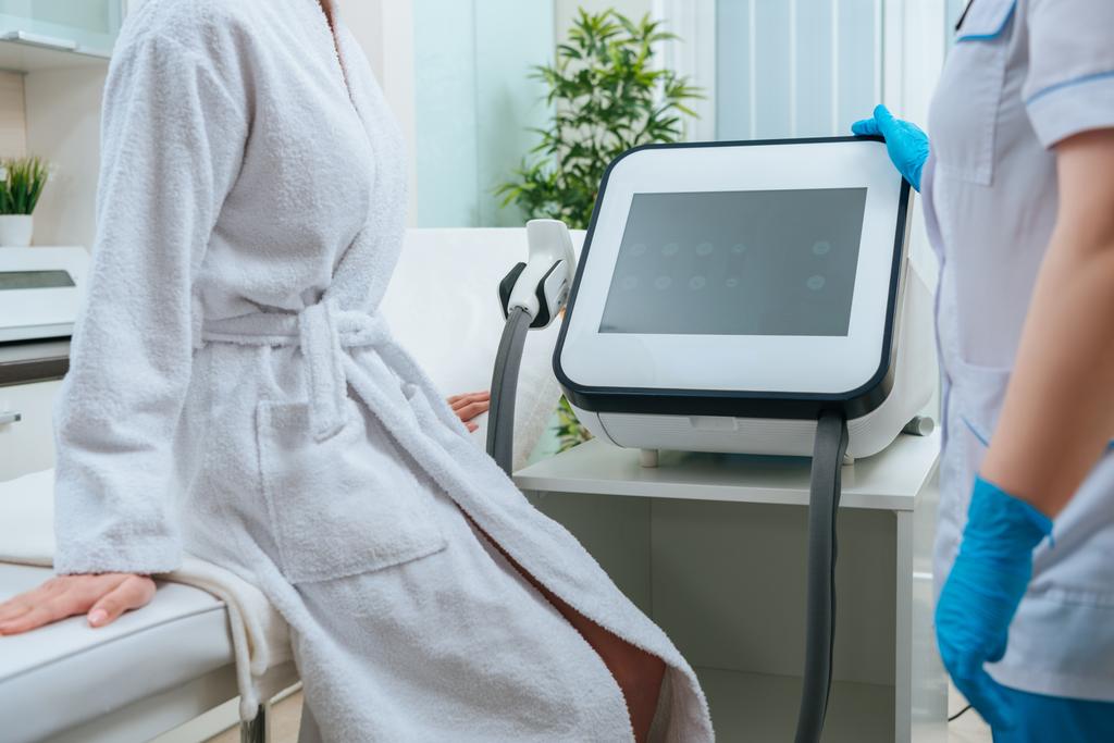 Частичный обзор косметолога в резиновых перчатках, касающихся лазерной машины в клинике
 - Фото, изображение