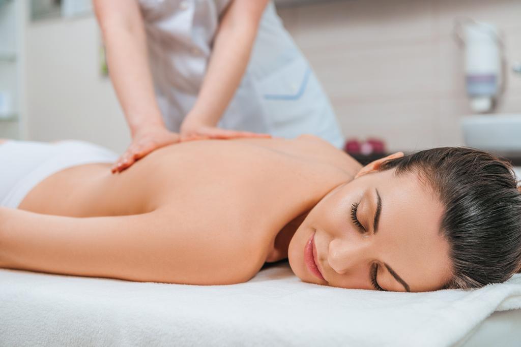 Частичный вид массажера, делающего массаж спины девушке на массажном столе
 - Фото, изображение