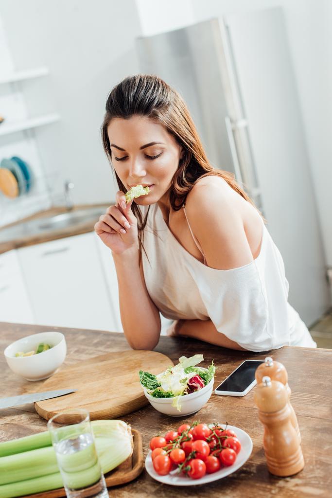 Chica pensativa sentada en la mesa y comiendo ensalada en la cocina
 - Foto, Imagen