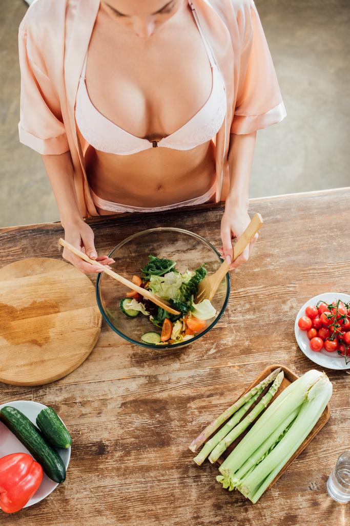 High angle view of woman in underwear and housecoat cooking vegetable salad in kitchen - Photo, Image