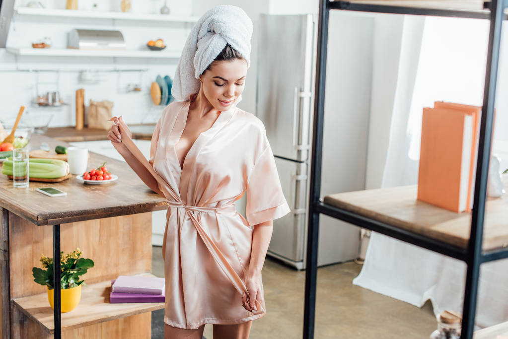 Młoda kobieta w housecoat z ręcznikiem na głowie patrząc w kuchni - Zdjęcie, obraz