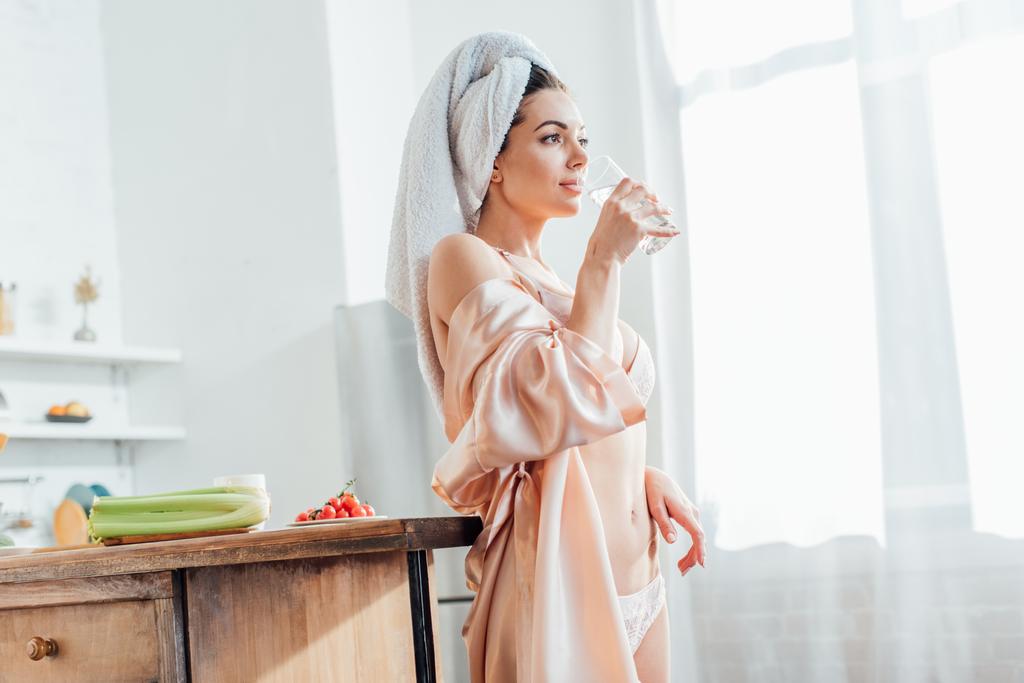 Sexy dívka v bílém prádle a v kabátě se sklenicí vody v kuchyni - Fotografie, Obrázek