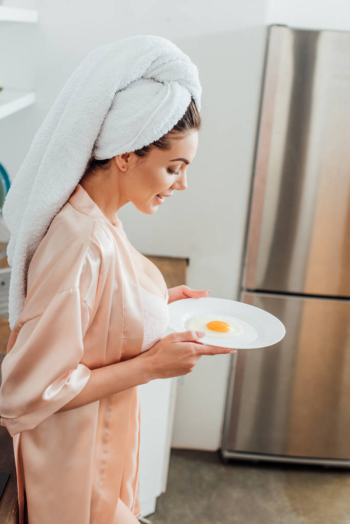 Side näkymä seksikäs nainen housecoat tilalla levy paistettu muna keittiössä
 - Valokuva, kuva