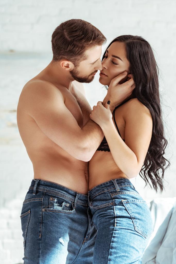 schöner und hemdloser Mann in Jeans umarmt schöne Frau in BH im Schlafzimmer  - Foto, Bild
