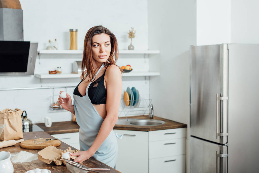 Seksikäs nainen alusvaatteet ja sininen esiliina tilalla munat keittiössä
 - Valokuva, kuva