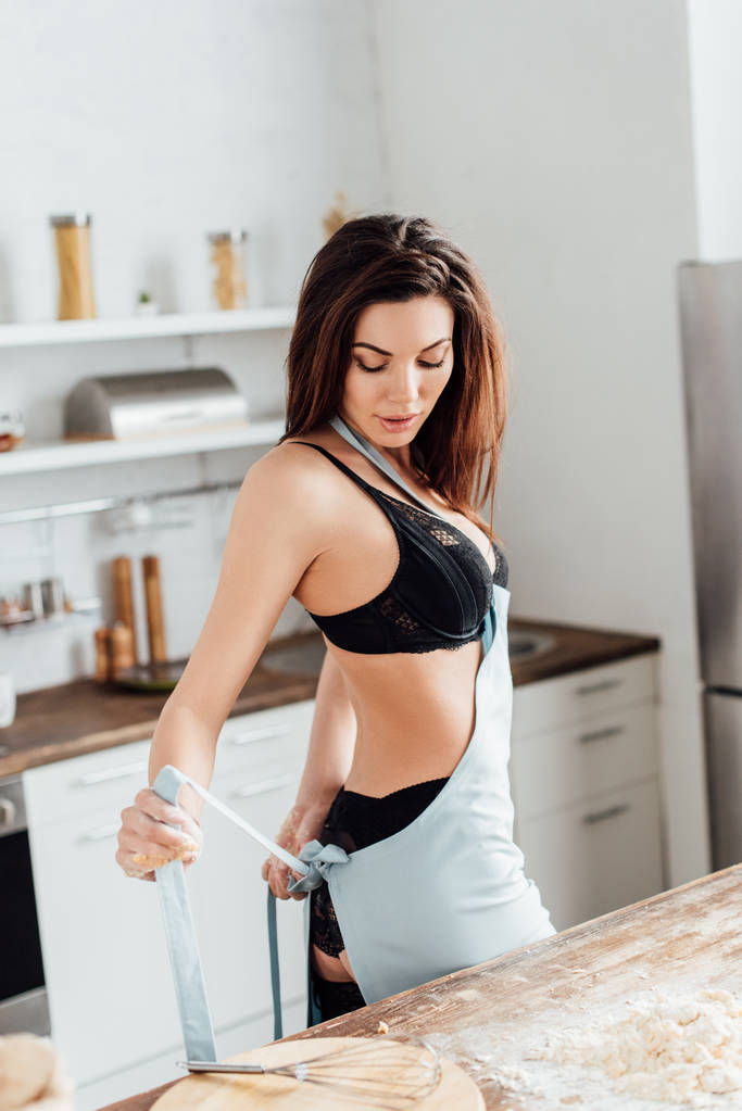 Mulher sexy em lingerie preta decolando avental na cozinha
 - Foto, Imagem