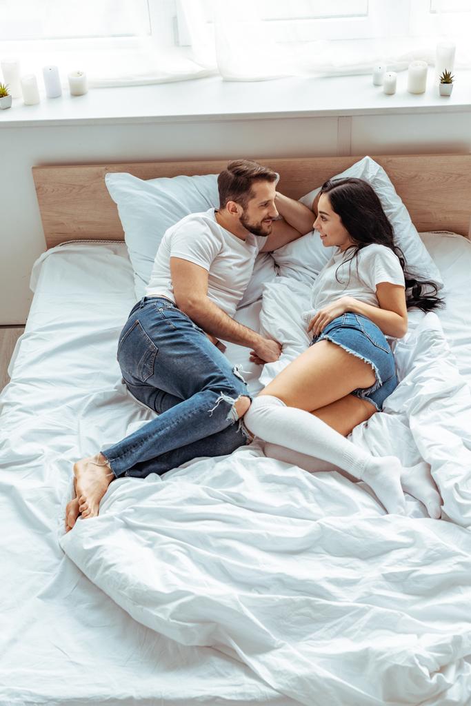 красивый мужчина и красивая и улыбающаяся женщина в белой футболке смотрят друг на друга в спальне
  - Фото, изображение