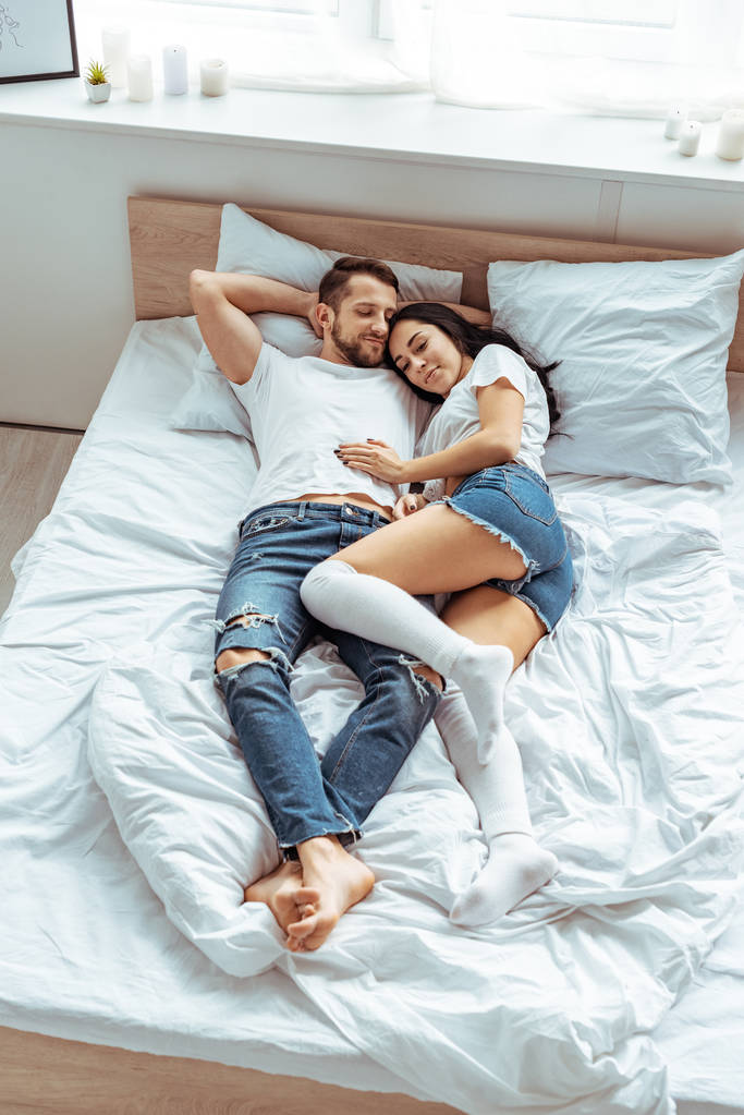 handsome man in jeans and beautiful and smiling woman hugging in bedroom  - Photo, Image