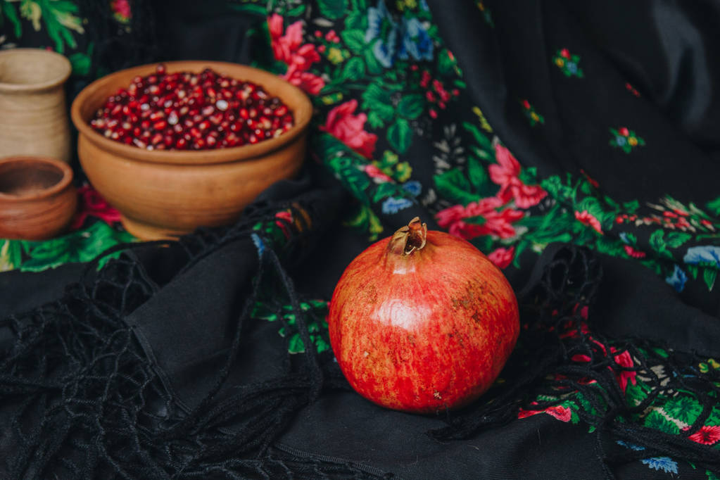 Granatapfelkörner in einer Keramikschale auf Vintage-Stoff-Hintergrund, Granatapfelfrüchte, Keramikkrug, Keramikteller, Ethno-Schal, Romma-Schal, Stillleben - Foto, Bild