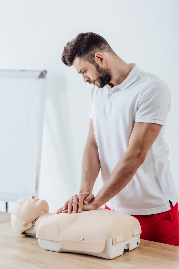 schöner Mann mit Brustkompressionstechnik auf Dummy während des CPR-Trainings  - Foto, Bild
