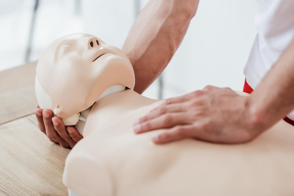 bijgesneden weergave van man met dummy tijdens het beoefenen van reanimatie tijdens eerste hulp training - Foto, afbeelding