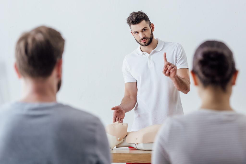 schöner Ausbilder mit CPR-Attrappe, der beim Erste-Hilfe-Kurs mit dem Finger zeigt - Foto, Bild