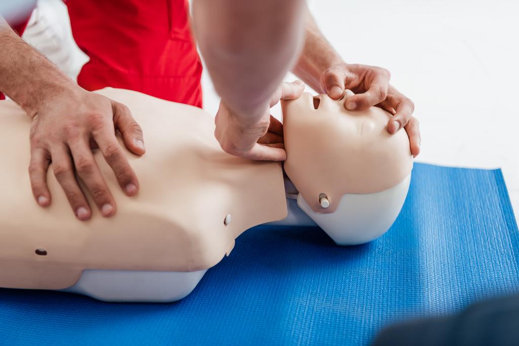 обрезанный взгляд мужчин, практикующих технику CPR на манекен во время обучения первой помощи
 - Фото, изображение