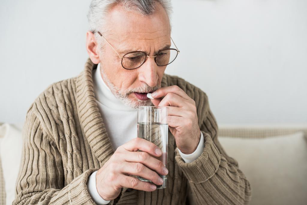 старший чоловік в окулярах приймає таблетки вдома
 - Фото, зображення