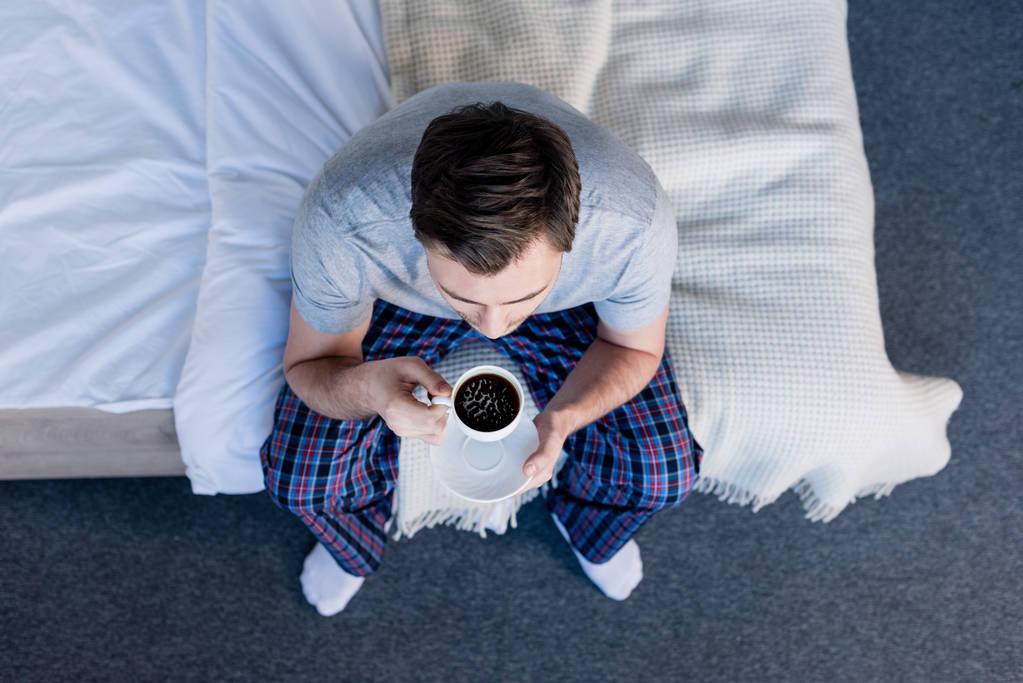 yatakta otururken pijamalar içinde adamın üst görünümü kahve tutan fincan - Fotoğraf, Görsel