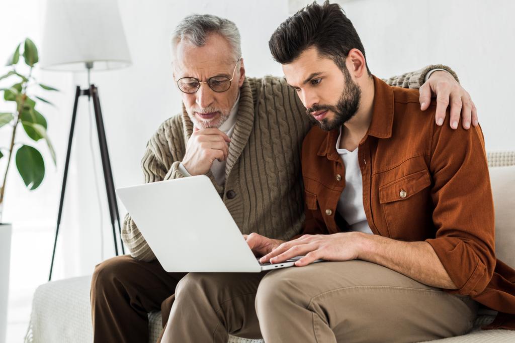 schöner Mann sitzt mit älterem Vater und schaut auf Laptop  - Foto, Bild