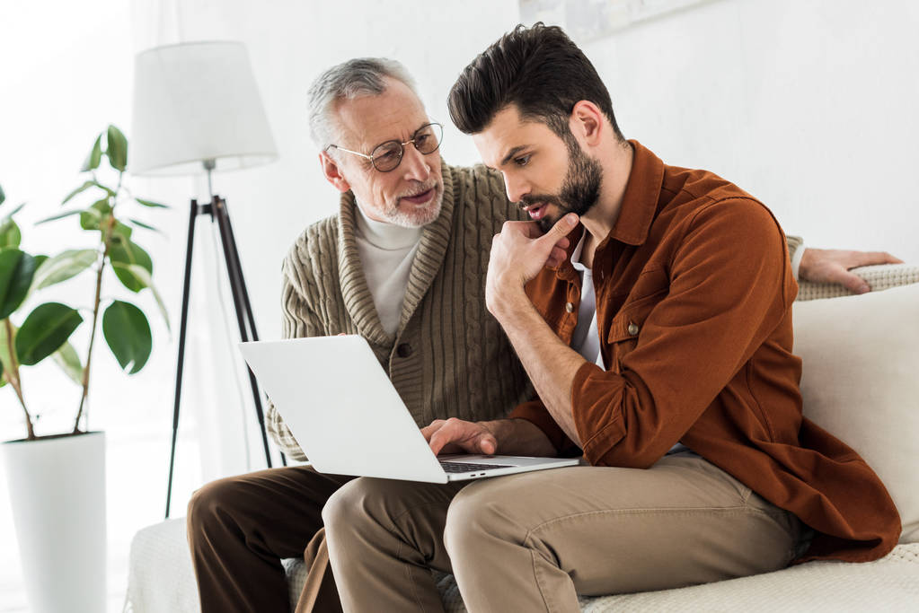 senior father looking at handsome son sitting with laptop  - Photo, Image