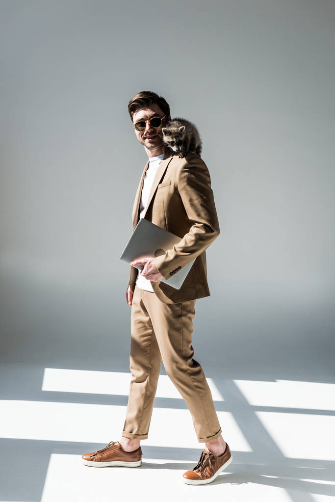 homem de boa aparência com guaxinim adorável no ombro segurando laptop em cinza
 - Foto, Imagem