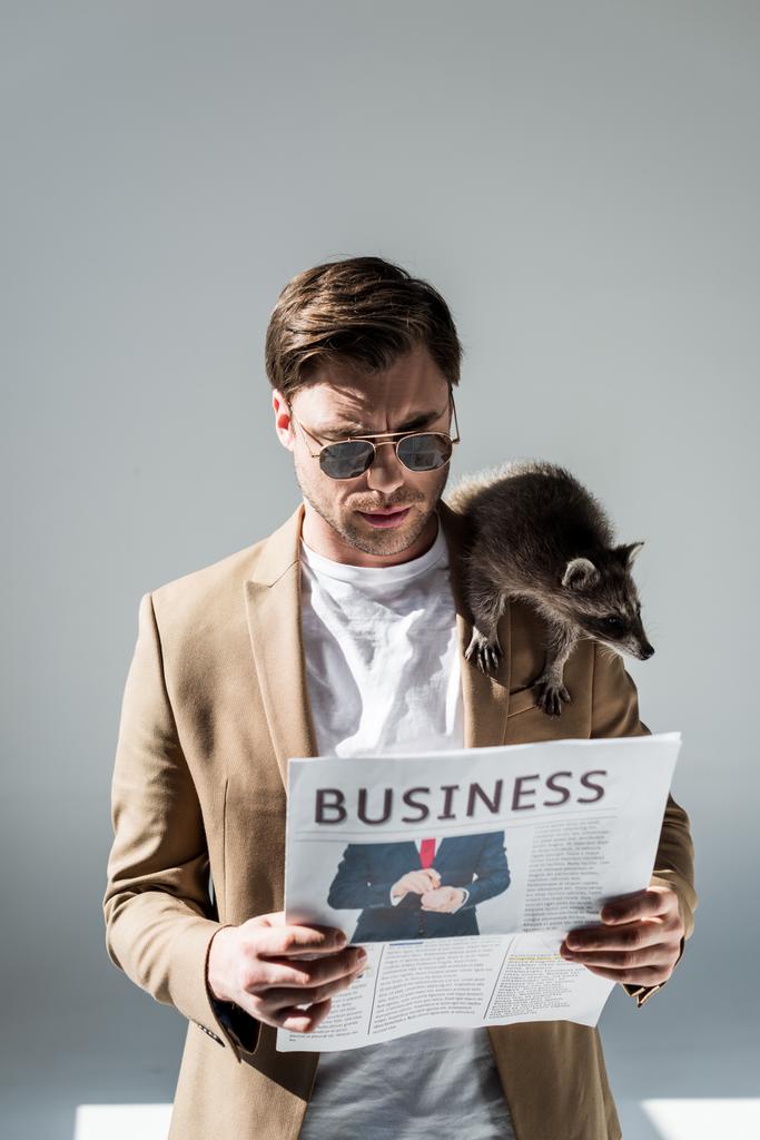 концентрований чоловік зі смішним єнотом на плечі читання бізнес-газети
 - Фото, зображення
