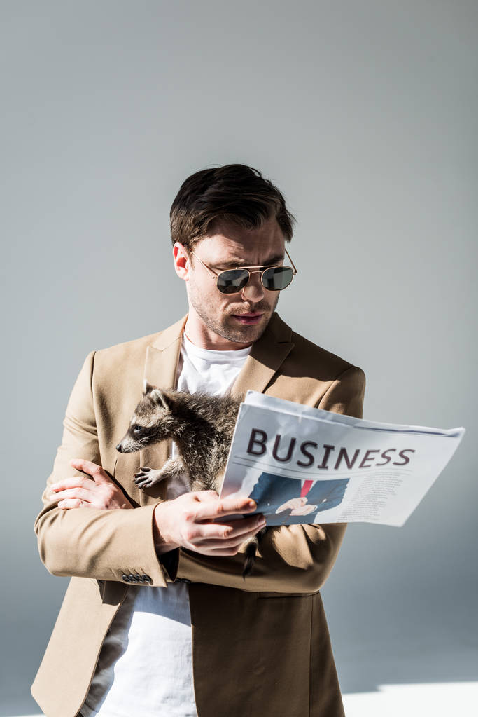 homme attentif dans les lunettes de soleil, avec raton laveur drôle sur l'épaule, lecture journal d'affaires
 - Photo, image