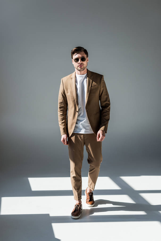 hombre de buen aspecto elegante en suite beige y gafas de sol de pie en la luz del sol en gris
 - Foto, imagen