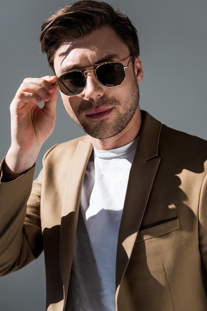 впевнений модний чоловік в сонцезахисних окулярах дивиться на камеру на сірому
 - Фото, зображення