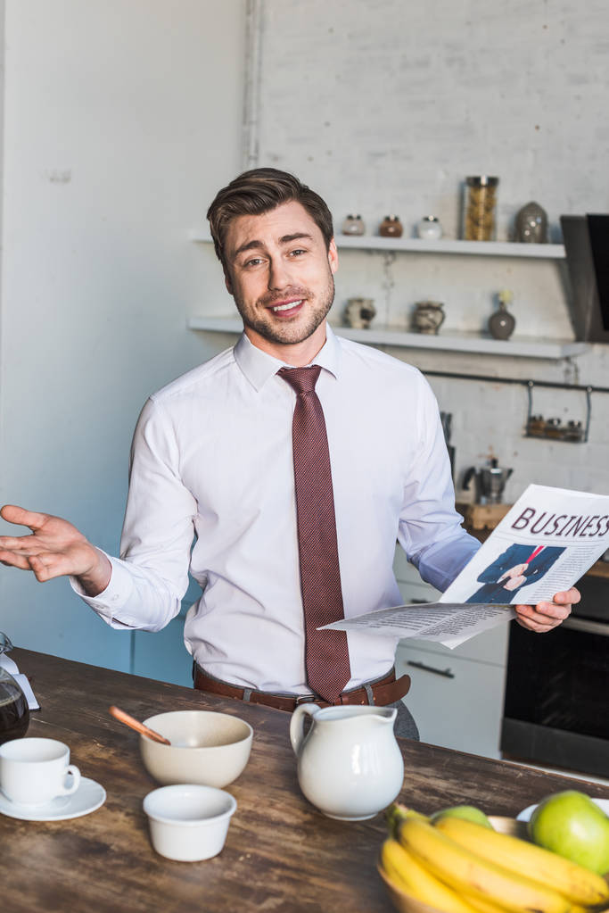 handsome man standing by kitchen table, holding business newspaper and looking at camera   - Photo, Image
