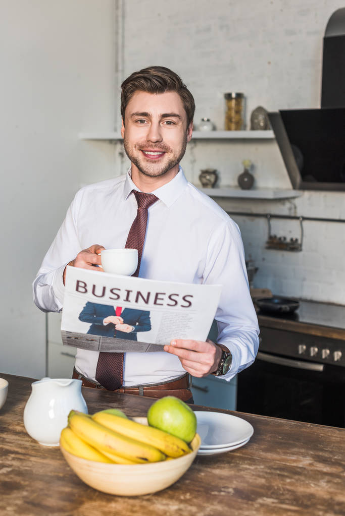 cheerful man holding business newspaper and coffee cup while looking at camera - Photo, Image