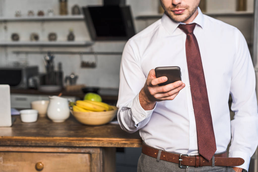 vista parcial del hombre usando el teléfono inteligente mientras está de pie en la cocina en casa
 - Foto, Imagen