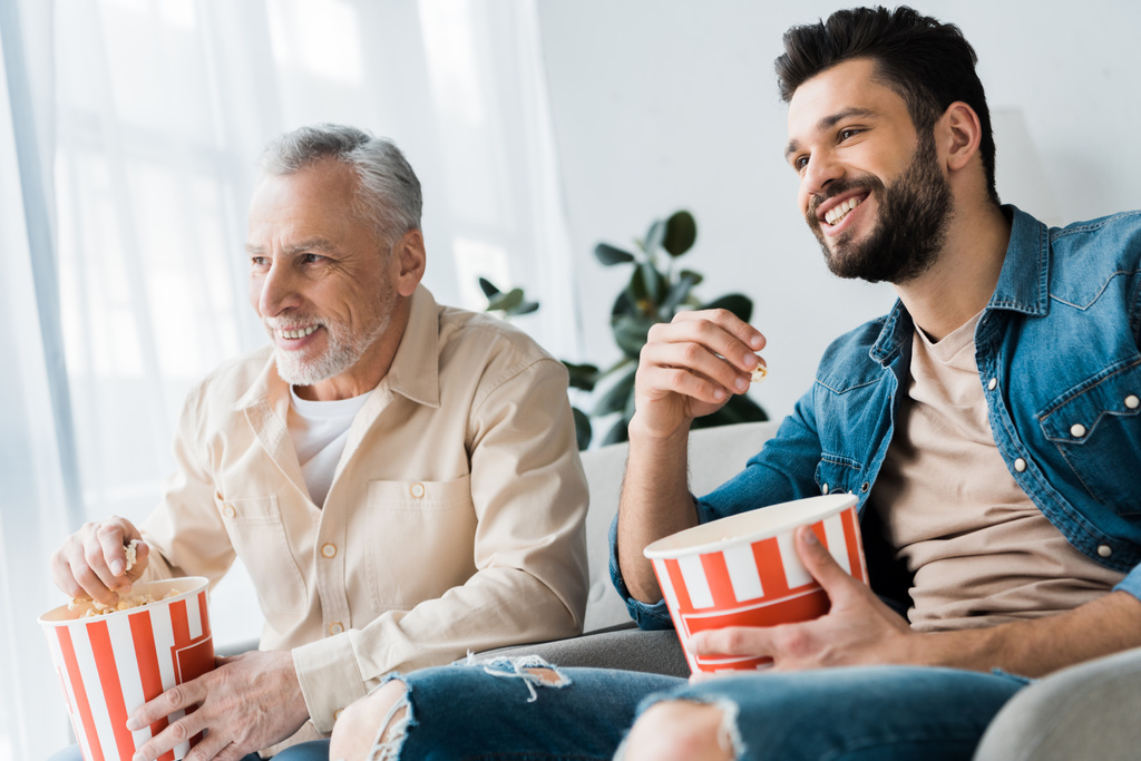 heureux père retraité assis avec son fils et tenant seau de maïs soufflé tout en regardant la télévision
 - Photo, image