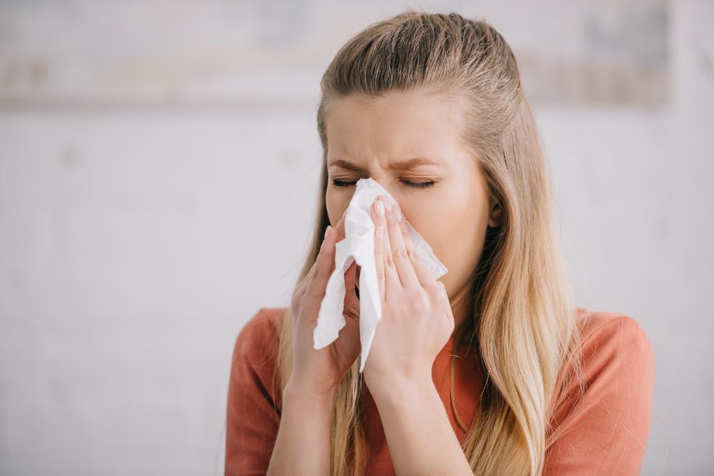 blonde woman sneezing while holding tissue near nose  - Photo, Image