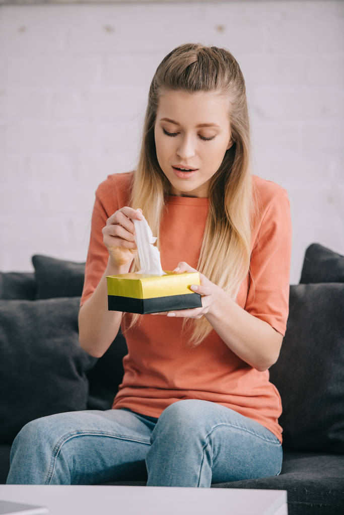blonde woman holding tissue box while sitting on sofa at home  - Photo, Image