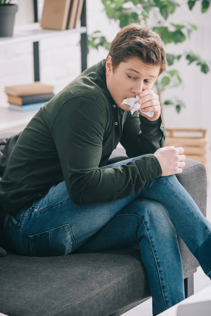 hombre guapo sosteniendo tejido mientras estornuda en casa
  - Foto, Imagen