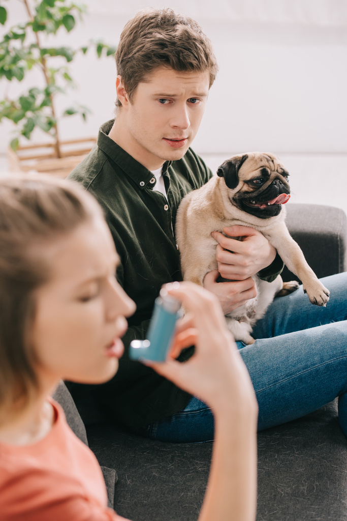 селективный фокус мужчины, держащего очаровательного мопса и глядя на женщину с аллергией на собаку с помощью ингалятора
  - Фото, изображение