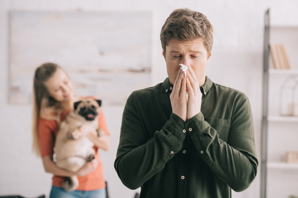 Selektywny fokus człowieka kichanie w tkanki z zamkniętymi oczami, stojąc w pobliżu kobieta z psem  - Zdjęcie, obraz
