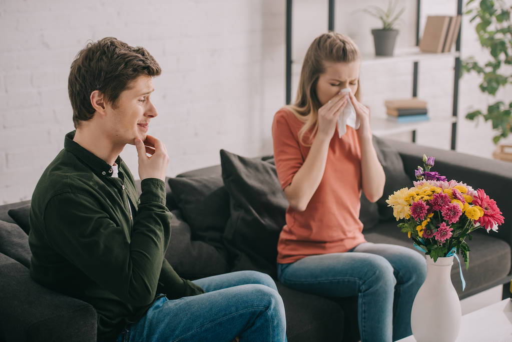 pensive man looking at vase with flowers near sneezing blonde girl with pollen allergy - Photo, Image
