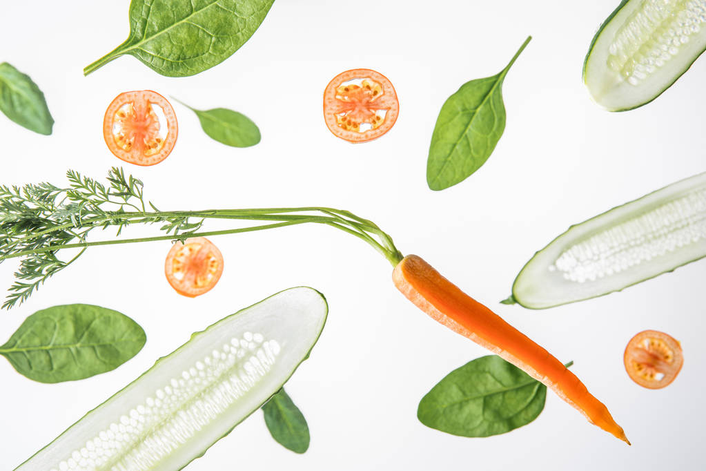 sliced cucumbers, tomatoes, carrot and spinach leaves on grey background - Photo, Image
