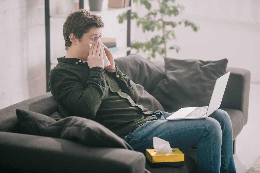 zieke man met allergie en niezen in een weefsel tijdens het gebruik van laptop  - Foto, afbeelding