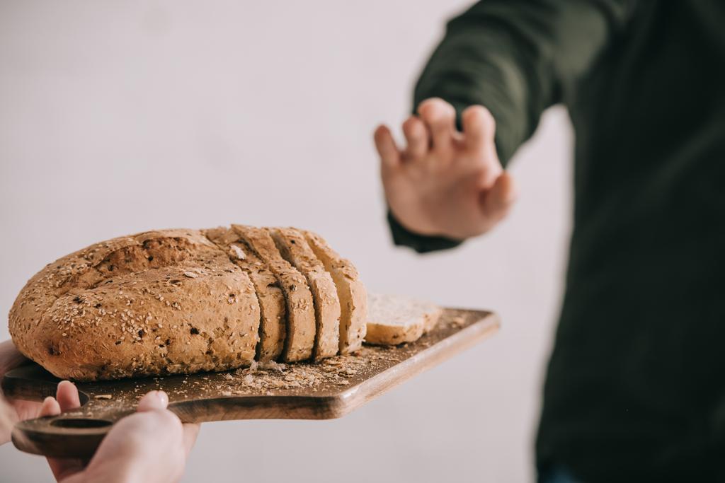 kırpılan görünümü gri izole gluten intoleransı ile kesme tahtası ile man yakınındaki dilimlenmiş ekmek tutan kadın - Fotoğraf, Görsel