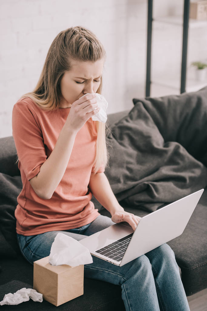 atractiva mujer rubia estornudando en el tejido mientras usa el ordenador portátil en casa
  - Foto, Imagen